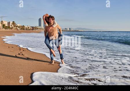 Mann Huckepack verspielte Frau, während am Strand stehen Stockfoto