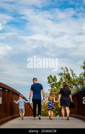 Eltern halten die Hände der Kinder, während sie auf dem Steg gegen Wolken laufen Himmel Stockfoto