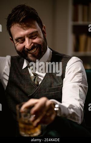 Porträt eines bärtigen Mannes, der lachend ein Glas Whiskey genießt Stockfoto