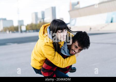 Spielerischer Mann Huckepack fröhlicher Freund beim Spielen im Freien Stockfoto