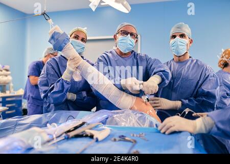 Ärzte Team mit Endoskop Ausrüstung Operation Schulter arthroskopische Chirurgie in Operationsraum während der COVID-19 Stockfoto