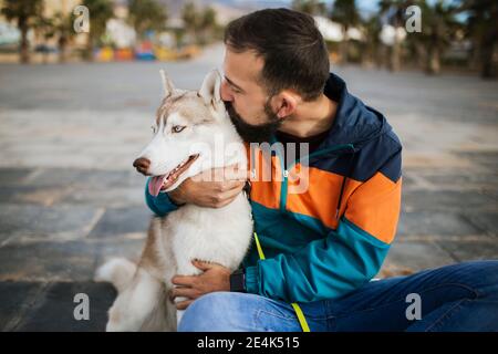 Bärtiger Mann küsst sibirischen Husky, während auf der Straße sitzen Stockfoto