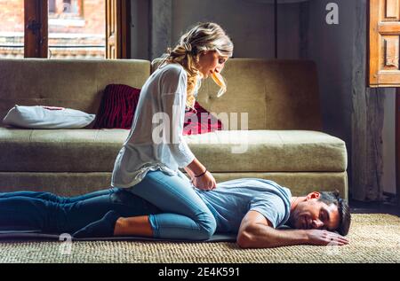 Junge Frau massiert Freund liegend auf Teppich im Wohnzimmer Zu Hause Stockfoto