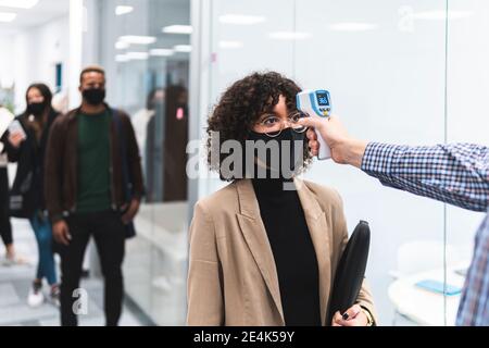 Weibliche professionelle geht durch Temperaturkontrolle, bevor sie zur Arbeit gehen Im Büro Stockfoto