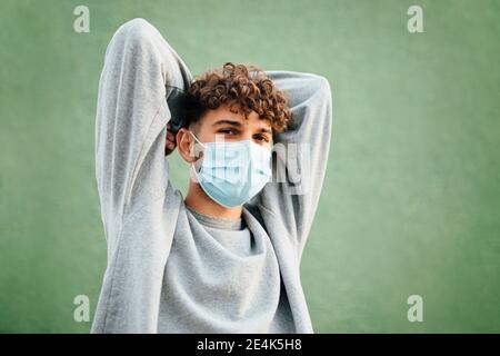 Junger Mann mit Händen hinter dem Kopf gegen grünen Hintergrund während Coronavirus Stockfoto