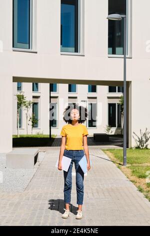 Junge Studentin, die Bücher hält, während sie mit geschlossenen Augen steht universität Stockfoto