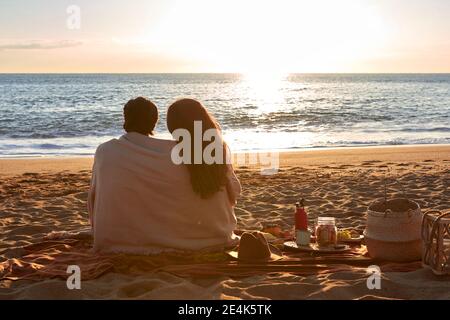Junges Paar mit Decke bedeckt Blick auf die Ansicht während des Sitzens Am Strand Stockfoto