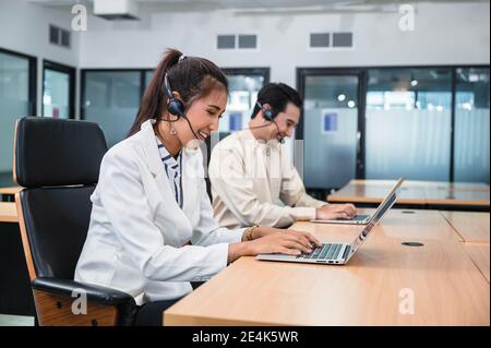 Junge asiatische Betreiber Frau Agent mit Headsets und Kollegen arbeiten Kundendienst in einem Callcenter Stockfoto