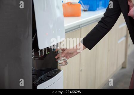 Frau Hand hält Glas füllen kaltes Wasser aus Wasserspender Stockfoto