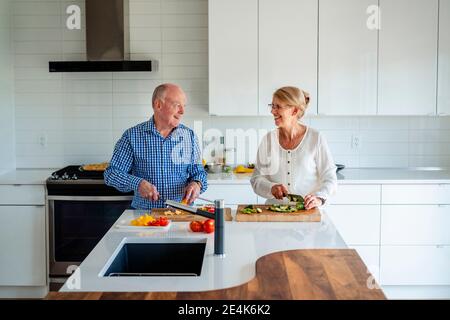 Ältere Pärchen reden während sie Gemüse auf Kücheninsel hacken Zu Hause Stockfoto