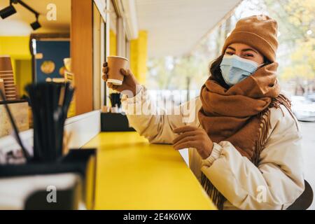 Junge Frau, die im Herbst Kaffee aus dem Straßencafé kauft COVID-19 Stockfoto