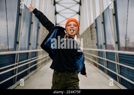 Glückliche junge Frau mit geschlossenen Augen heraus ragen Zunge während tanz auf dem Steg Stockfoto