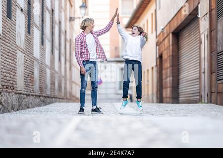 Junger Mann, der beim Aufstehen High-Five an aufgeregt Junge gibt Fußweg Stockfoto