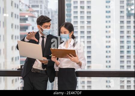 Multiethnische Geschäftskollegen tragen Gesichtsmaske Diskussion und Beratung mit Laptop in neuen normalen Büro im Geschäftsviertel. Während Pandemie von C Stockfoto