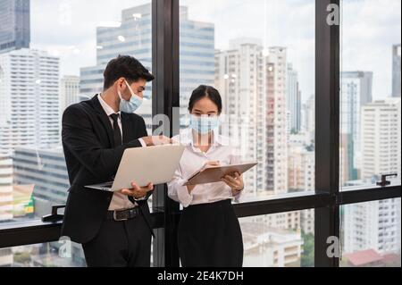 Multiethnische Geschäftskollegen tragen Gesichtsmaske diskutieren und Beratung in neuen normalen Büro im Geschäftsviertel. Während Pandemie des Coronavirus, Stockfoto