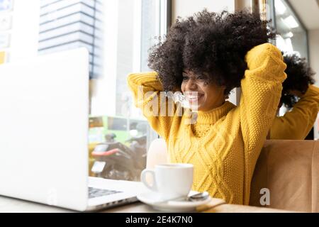 Lächelnde Frau mit Händen hinter dem Kopf, die im Café sitzt Stockfoto