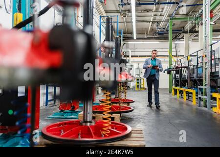 Reifer Geschäftsmann im Anzug arbeiten auf digitalen Tablet beim Gehen Im Werk Stockfoto