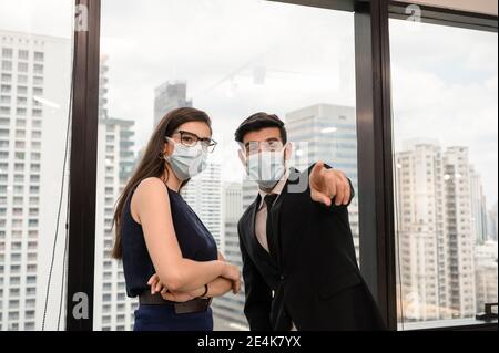 Junge kaukasische Geschäftskollegin mit Gesichtsmaske und Zeigefinger Im modernen Büro in der Innenstadt Stockfoto