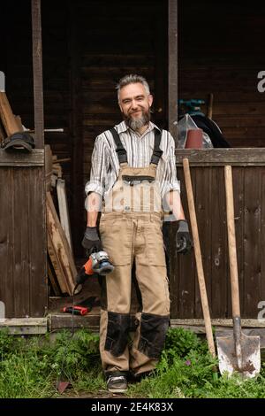 Porträt eines bärtigen Zimmermanns, der im Freien steht, mit Mühle in der Hand Stockfoto