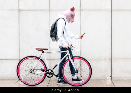 Junger Mann mit Smartphone zu Fuß mit dem Fahrrad auf dem Fußweg Stockfoto