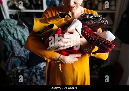 Kleider, die das Gesicht der Frau bedecken, während sie mit den Händen auf der Hüfte gegen den Kleiderständer im Kleiderschrank stehen Stockfoto