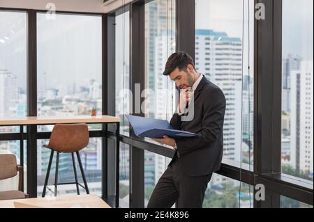 Kaukasischer Geschäftsmann in Anzug stehend mit halten Papierkram und Analyse Business-Plan in modernen Büro Stockfoto