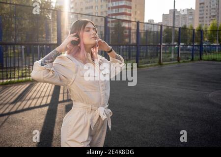 Junge Frau mit geschlossenen Augen, die Kopfhörer hält, während sie Musik hört Auf dem Sportplatz Stockfoto