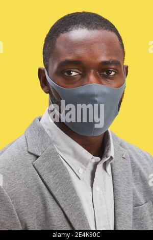 Vertikales Kopf- und Schulterporträt eines afroamerikanischen Mannes mit Maske Und die Kamera betrachten, während sie vor knallgelbem Hintergrund steht Stockfoto
