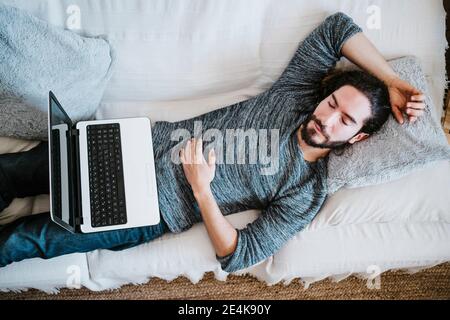 Mann mit Laptop schläft zu Hause auf dem Sofa Stockfoto