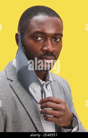 Vertikales Porträt eines afroamerikanischen Mannes, der die Maske auszieht und schaut Bei der Kamera, während Sie vor knallgelbem Hintergrund stehen Stockfoto