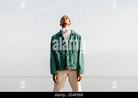 Junger afrikanischer Mann, der gegen Himmel und Meer steht Stockfoto