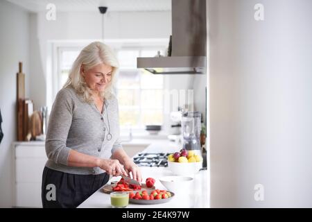 Rentnerin schneidet Erdbeeren an Bord in der Küche zu Hause Stockfoto
