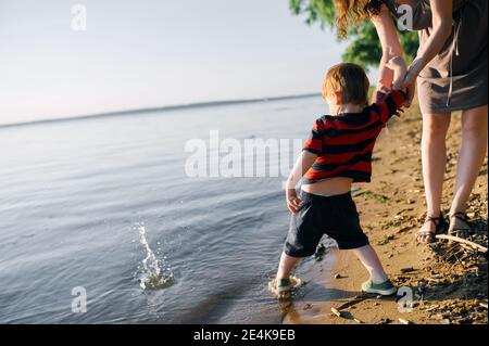 Ein kleines Kind spielt am Ufer des Sees Und tauche seinen Fuß mit seiner Mutter ins Wasser Stockfoto