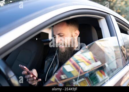 Bärtiger Mann mit Handy, während er im Auto saß gesehen Durchgangsfenster Stockfoto