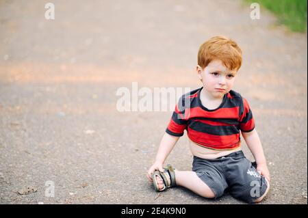 Kleiner Junge sitzt im Sommer auf dem Boden in Der Park und weint Stockfoto