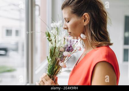 Frau riecht Blumen am Fenster Stockfoto