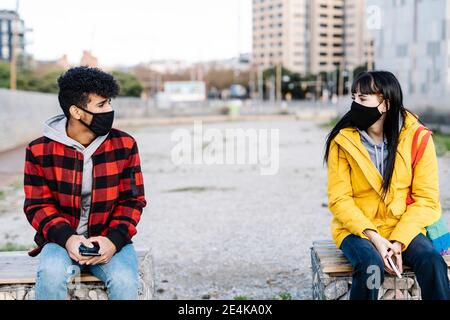 Paar trägt eine schützende Gesichtsmaske, die in sozialer Distanz sitzt Prüfstand während COVID-19 Stockfoto