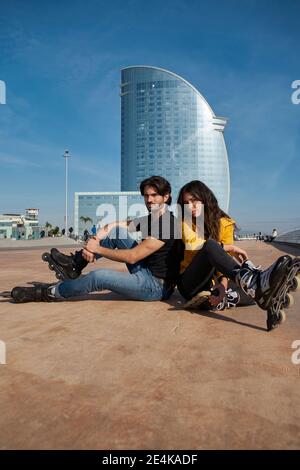 Junger Mann und junge Frau sitzen am Pier gegen den Himmel Stockfoto