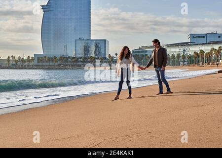 Junges Paar, das Hände hält, während es am Strand läuft Stockfoto