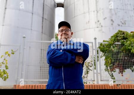 Älterer männlicher Winzer mit gekreuzten Armen gegen Edelstahlfass In der Weinindustrie Stockfoto