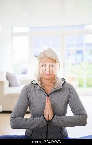 Lächelnde ältere Frau mit Händen zusammengeklemmt Ausübung zu Hause Stockfoto