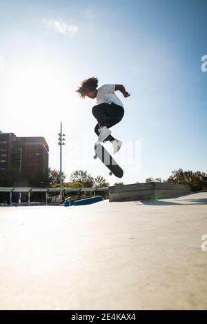 Lockiges Haar Mann tun Kickflip mit Skateboard an sonnigen Tag Stockfoto