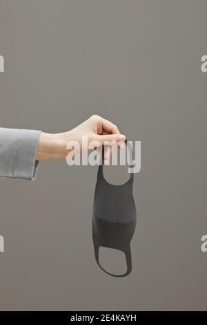 Grafikbild der weiblichen Hand halten Maske vor minimalem grauen Hintergrund, Copy Space Stockfoto
