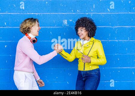 Fröhliche multiethnische Freunde lachen, während sie die Hand gegen Blau halten Wand Stockfoto