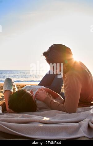 Mann, der die Hand auf die Frau hält, die auf der Decke liegt, während er sich ausruhte Am Strand Stockfoto