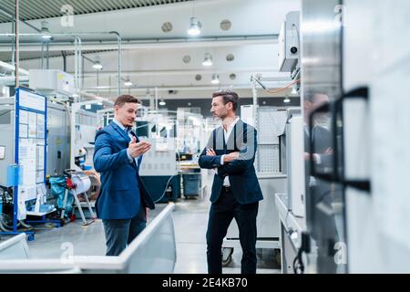 Geschäftsleute diskutieren, während in der Fabrik von Maschinen umgeben stehen Stockfoto