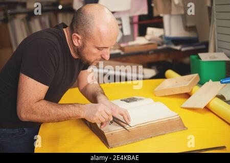 Buchbinder stellt altes Buch in Handwerkswerkstatt wieder her Stockfoto