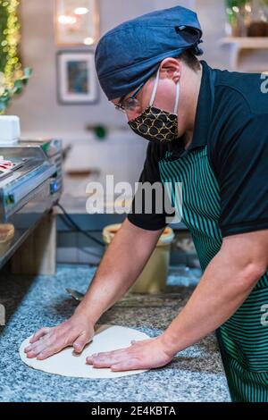 Männlicher Koch trägt Schutzmaske Vorbereitung Pizzateig Stockfoto