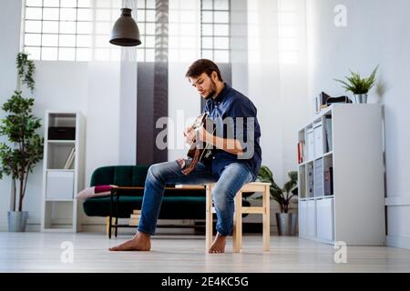 Professionelle Probenarbeit mit Gitarre, während Sie auf dem Hocker sitzen studio Stockfoto