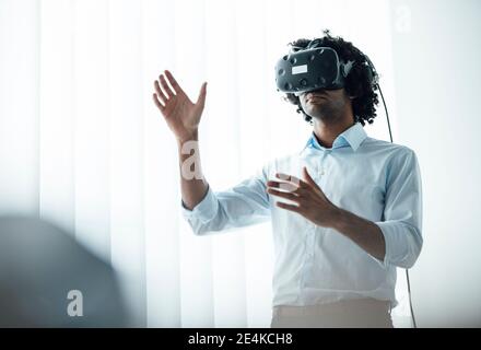 Junger Geschäftsmann trägt Virtual-Reality-Headset, während er an Bord gestikelt Zimmer im Büro Stockfoto